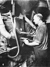 焙煎釜からのサンプラーによる焙煎豆のサンプリングの様子。左手には焙煎度を確認する標準豆トレイ。All about Coffee 1922より。