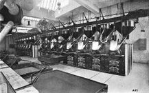 図6:1900年頃の16機のバーンズ焙煎機を使用したニューヨークのFischer&Co.の焙煎設備。手前の箱は吸引式冷却機 (Cooking carと呼ばれ移動して使用)。All About Coffee 1922年より。